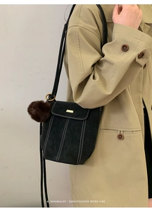 Detail of black suede bucket bag with white contrast stitching and plush ball charm