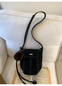 Detail of black suede bucket bag with contrast stitching and brown plush ball charm