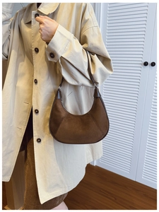 Brown suede crescent shoulder bag in minimalist patchwork design worn with beige coat