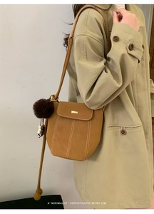 Detail of caramel suede bucket bag with gold hardware and plush charm on trench coat