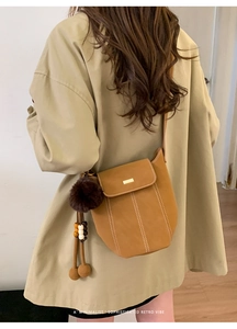 Detail of tan suede bucket bag with contrast stitching and decorative plush charm
