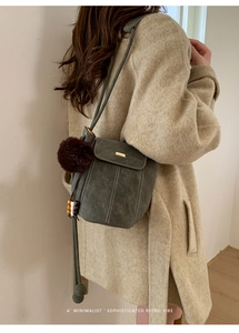 Detail of dark green retro bucket bag with plush pompom charm and metal snap closure