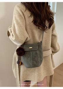 Detail of dark grey-green suede bucket bag featuring contrast stitching and plush charm
