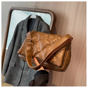 Close-up of brown quilted faux leather shoulder bag with wide strap and gold buckle