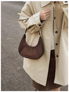 Brown suede crescent bag shown with a beige trench coat in an outdoor setting