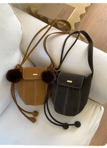 Detail of faux suede bucket bags in camel and dark coffee with decorative pom-poms
