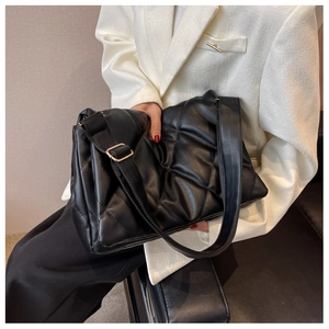 Close-up of black quilted shoulder bag with adjustable strap and golden metal buckle