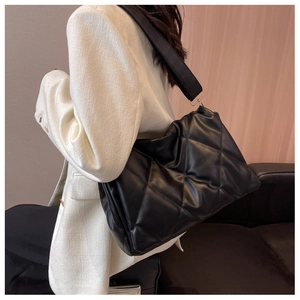 Detail of a black puffer quilted shoulder bag with silver hardware on a female model