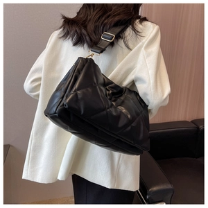 Detail of black quilted shoulder bag with golden buckle on a white blazer