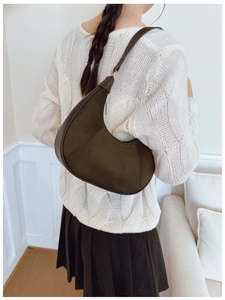 Detail view of a model wearing a dark green suede crescent bag over a white sweater