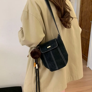 Minimalist black faux suede bucket bag with white stitching and decorative pompom charm