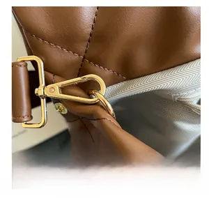Close-up of vintage gold metal hook on brown leather bag with herringbone lining