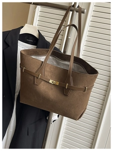 Détail d'un grand cabas en daim marron avec boucle dorée sur un fond de costume chic