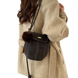 Brown suede bucket bag with white contrast stitching and faux fur pompom charm