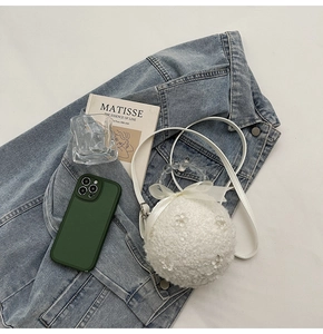 Detailed view of white faux fur crossbody bag with pearl handle and ribbon on denim jacket