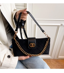 Close-up of black quilted suede handbag with gold interlocking rings and metal chain