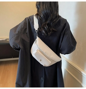 Detail view of a cream leather waist bag with lychee texture and fabric strap on a person