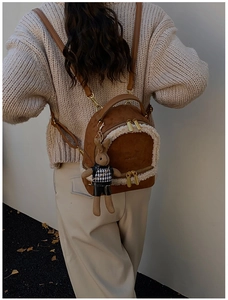 Brown mini backpack with plush shearling trim and cute rabbit charm on a model's back