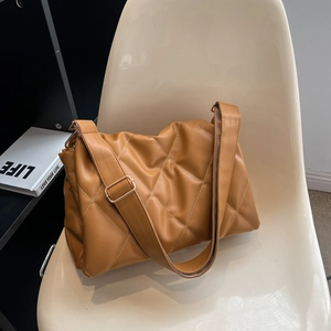 Caramel brown quilted crossbody bag with white stitching on a modern white chair