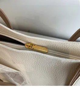 Detail of a smooth golden zipper pull on a beige lychee pattern leather tote bag
