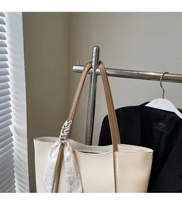 Detail of minimalist cream leather tote bag with silk scarf accent and brown shoulder strap