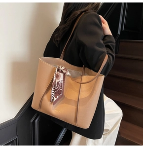 Large brown tote bag with printed silk scarf detail worn by a model in interior