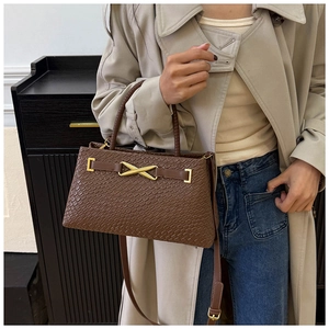 Détail du sac à main marron foncé texturé avec boucle métallique dorée en forme de X