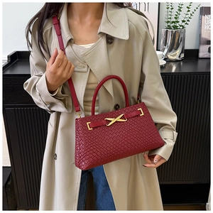Sac à main tissé rouge avec boucle dorée en X, porté sur un trench-coat beige élégant
