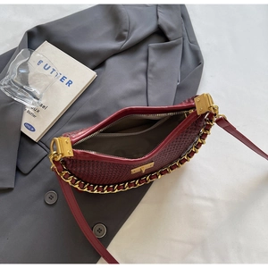 Détail d'un sac bordeaux à texture tissée avec chaîne dorée et poche intérieure zippée
