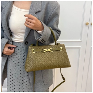 Détail d'un sac à main tressé vert foncé avec boucle dorée en X élégante et quincaillerie