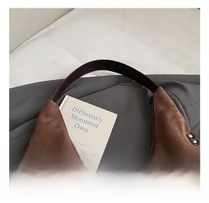 Detail showing the brown suede texture, leather strap, and vintage rivets of the tote bag