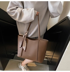 Detail of a brown tote bag with textured finish and a patterned silk scarf on handle