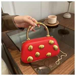 Detail of red leather handbag with golden metal accents and spiral top handle