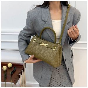 Détail d'un sac tressé vert olive avec une grande boucle métallique dorée en forme de X
