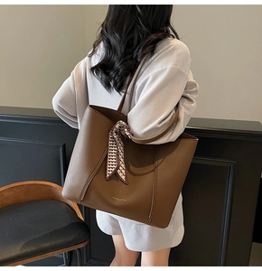 Detail of dark brown leather tote bag featuring a decorative scarf and fashion branding