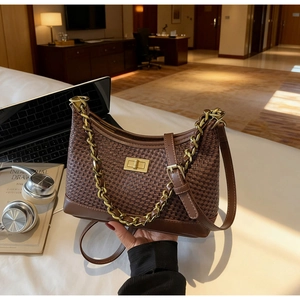 Détail d'un sac bandoulière tressé marron avec chaîne dorée et fermoir pivotant