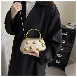 Detailansicht der goldfarbenen Abendtasche mit Kieselstruktur, Perlengriff und Kette