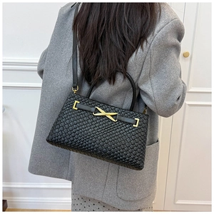Détail du sac tressé noir avec fermoir métallique en X doré et bandoulière en cuir
