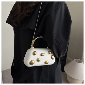 Close-up of white evening clutch featuring gold relief ornament and metallic chain strap
