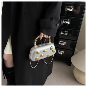 Detail of silver hard-shell evening bag with gold dots and spiral metal handle