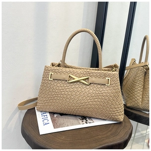 Détail du sac à main tissé beige avec boucle en X dorée sur un tabouret en bois foncé