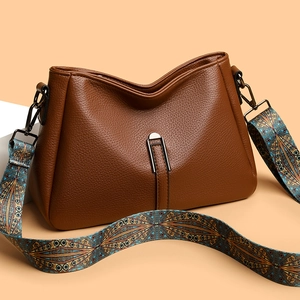 Brown leather crossbody bag with wide ethnic pattern strap and metal clasp on beige background