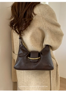 Détail du sac sous l'aisselle en cuir marron foncé avec fermoir doré sur manteau beige