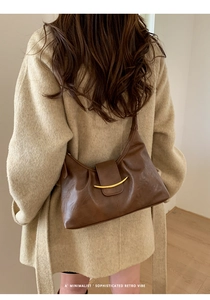 Détail d'un sac sous le bras en cuir marron foncé avec boucle métallique dorée en croissant