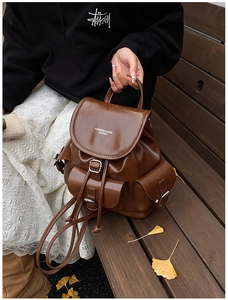 Detail of dark brown leather backpack with silver buckles and flap pockets on wood bench