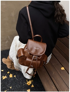 Brown faux leather backpack details with flip cover and decorative buckle in outdoor setting