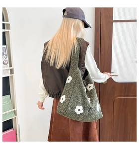 Detailed view of dark green knit tote bag with white floral patterns on model's shoulder