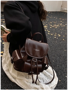 Outdoor shot of a vintage dark brown leather backpack with silver ginkgo leaves on the ground