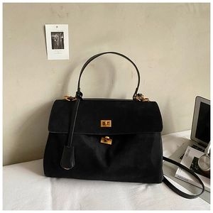 Close-up of black suede handbag featuring a gold twist lock and a textured surface