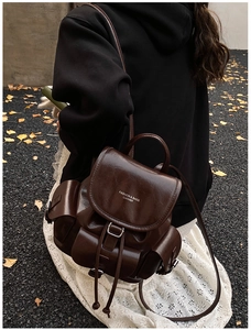 Detail of dark brown leather backpack with drawstring closure and metal buckle hardware